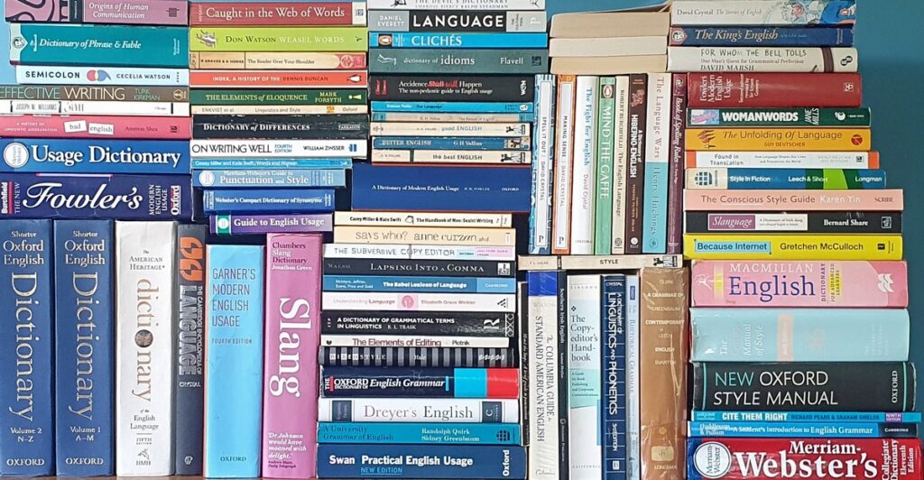 Several dozen books about language, of various sizes and colours, some stacked horizontally and others arranged vertically so that gaps between them are minimized. There are dictionaries, usage dictionaries, style guides, writing manuals, pop linguistics, and books about editing, spelling, punctuation, and so on.